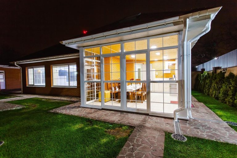 Stijlvolle veranda met houten constructie, helderglazen dak en comfortabel zitmeubel waar je buiten met allure kunt genieten.